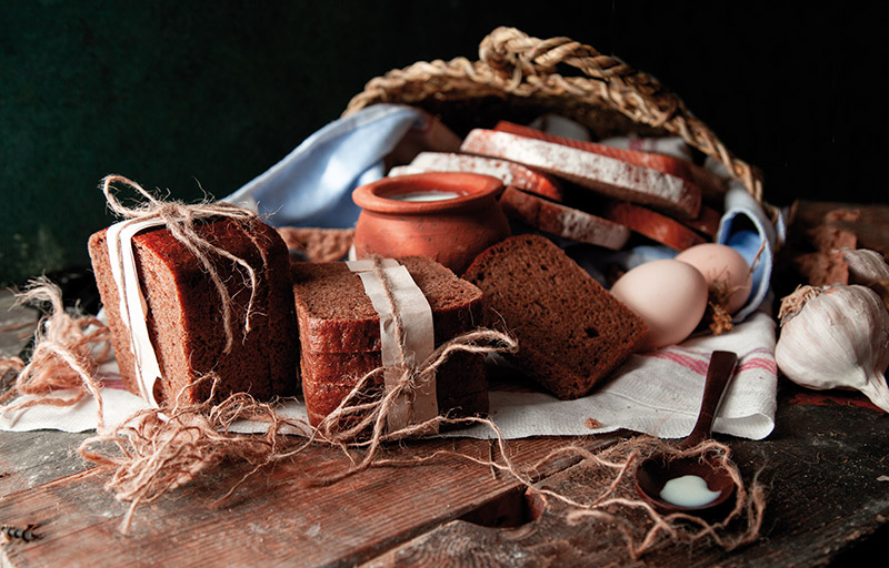 Black bread slices wrapped with white paper and tustic thread with a pot of milk, eggs and garlic on a white towel. image