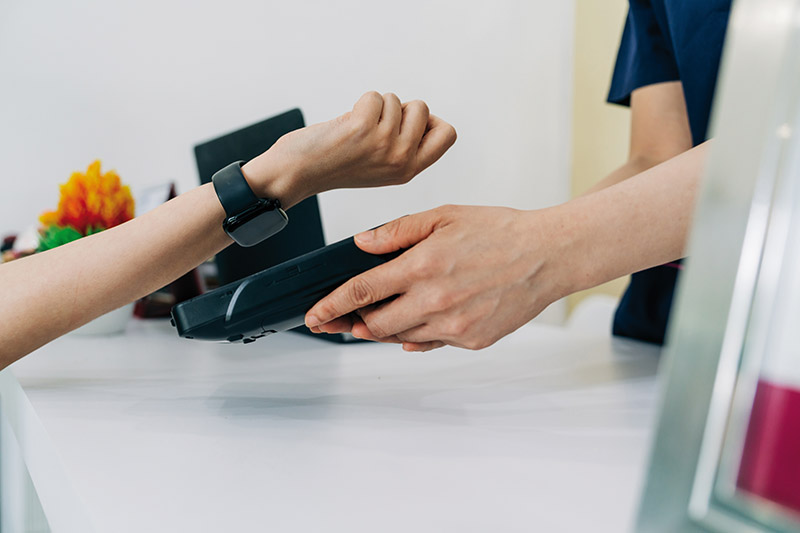 A professional uses a smartwatch for an NFC payment at a modern reception counter. Wearable payment technology makes transactions efficient and effortless.
